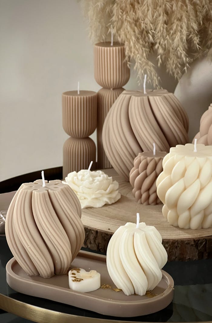A collection of intricately designed handmade candles in beige and creamy tones on a wooden surface.