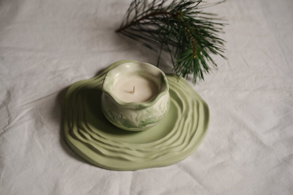 A stylish handmade green ceramic candle holder displayed with pine branches adds a rustic touch.