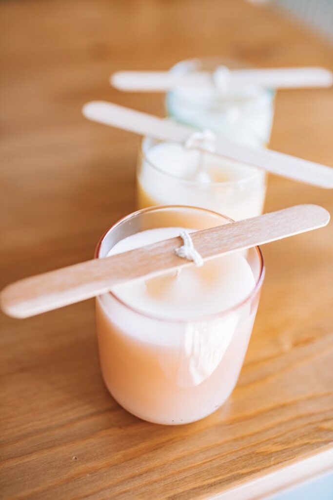 Close-up of handmade scented candles in glass jars with wooden wicks on a wooden table.