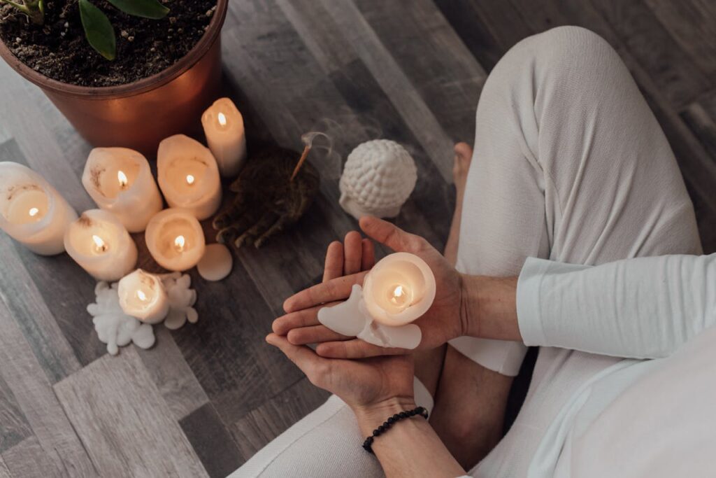 Top view of a person holding a candle in a serene setting, surrounded by lit candles on a wooden floor.