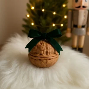 Small walnut-shaped decorative jar with dark green velvet ribbon bow, displayed on white faux fur with Christmas tree and nutcracker in background