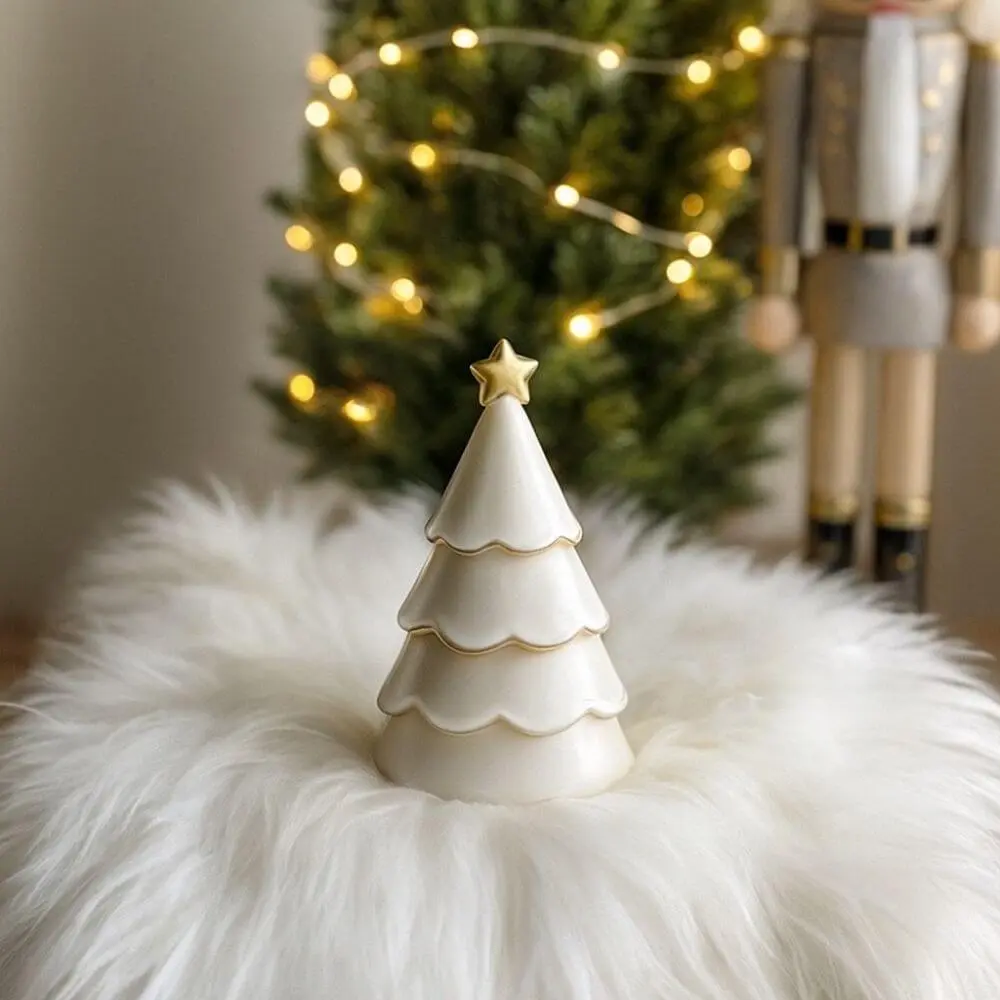 White Christmas tree candle with golden star topper, displayed on soft faux fur with warm festive lights and Christmas tree in background