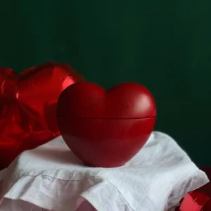 Hand-poured red heart-shaped candle for Valentine’s Day, romantic handmade gift idea for him or her, perfect for creating cozy and intimate atmosphere, styled with red heart balloons and festive ribbon.