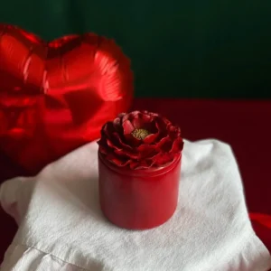 Romantic red candle with sculpted camellia flower lid, perfect Valentine’s Day scented gift, surrounded by red heart-shaped balloons, handmade floral candle for her, luxury holiday decor for love celebration.