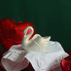 White swan-shaped handmade aroma candle styled with red heart balloons and white cloth – perfect romantic decor or gift for Valentine’s Day or anniversary celebration.