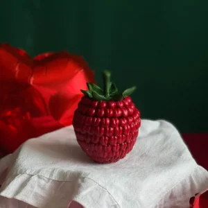 Realistic raspberry-shaped aroma candle with green leaves, styled for Valentine’s Day with red heart balloons and white cloth – perfect handmade gift for a romantic celebration.