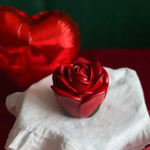 Handmade red rose-shaped aroma candle, perfect romantic gift for Valentine’s Day, elegant floral wax decor surrounded by heart-shaped balloons and red festive setting.