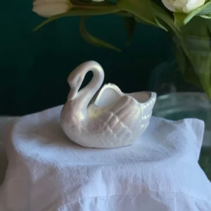 Elegant white swan-shaped candle on soft fabric with flowers in the background, handmade decorative candle for International Women’s Day, feminine home decor and thoughtful March 8 gift.