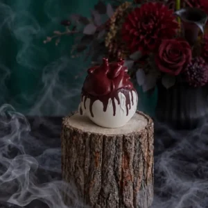 Handmade anatomical heart scented candle with dark red wax drips, styled with smoky Halloween decor and deep red flowers.