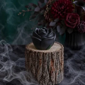 Handmade black rose-shaped scented candle with green leaf details, styled with smoky Halloween decor and dark red flowers.
