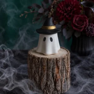 Handmade white ghost-shaped scented candle wearing a black witch hat with gold trim, styled with smoky Halloween decor.