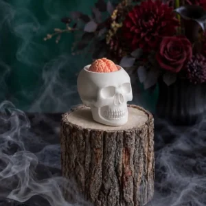 Handmade white skull-shaped scented candle with a pink brain detail, styled with smoky Halloween decor.