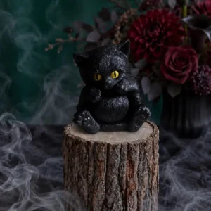 Handmade black cat-shaped scented candle with bright yellow eyes, styled with smoky Halloween decor.