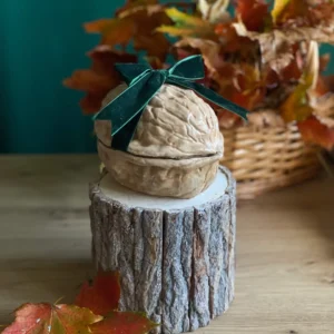 Handmade scented walnut-shaped candle with a dark green velvet bow, styled with autumn leaves on a rustic wood stand.