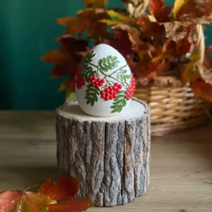 Handmade scented egg-shaped candle with red berry and green leaf details, styled with autumn leaves.