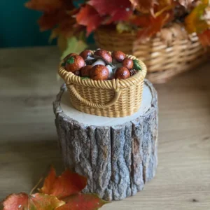 Handmade scented candle shaped like a wicker basket filled with mushrooms, styled with autumn leaves on a rustic wood stand.