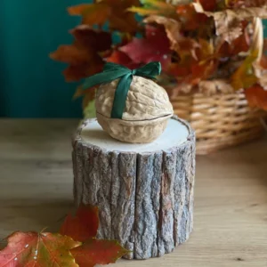 Handmade scented walnut-shaped candle tied with a dark green bow, styled with autumn leaves on a rustic wood stand.