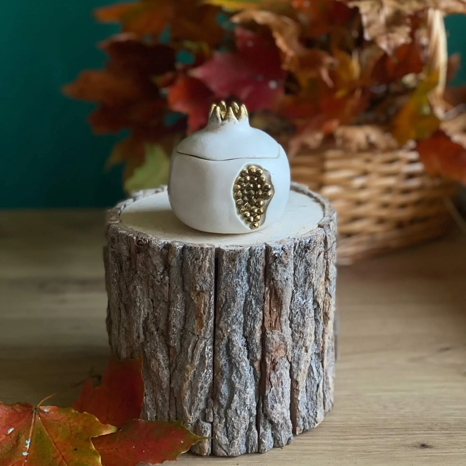 Handmade scented white pomegranate-shaped candle with gold accents, styled with autumn leaves on a rustic wood stand.