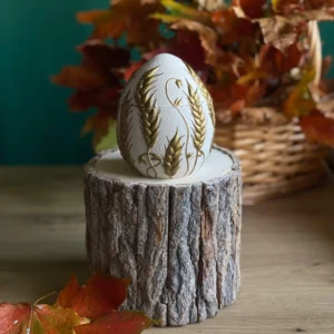 Handmade scented egg-shaped candle with raised golden wheat details, styled with autumn leaves on a rustic wood stand.