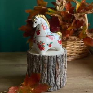 Handmade scented horse-shaped candle with apple details and gold accents, styled with autumn leaves.