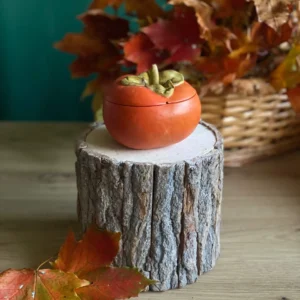 Handmade scented persimmon-shaped candle in warm orange with gold leaf details, styled with autumn leaves.