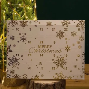 24-day wax melt advent calendar with numbered doors and gold snowflake design, displayed beside a lit Christmas tree.