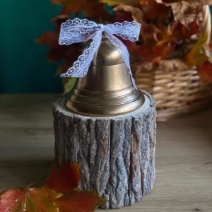 Handmade scented bell-shaped candle in metallic gold with a white lace bow, styled with autumn leaves.
