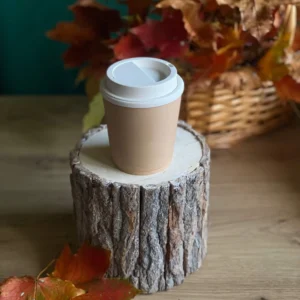 Handmade scented candle shaped like a takeaway coffee cup, styled with autumn leaves on a rustic wood stand.